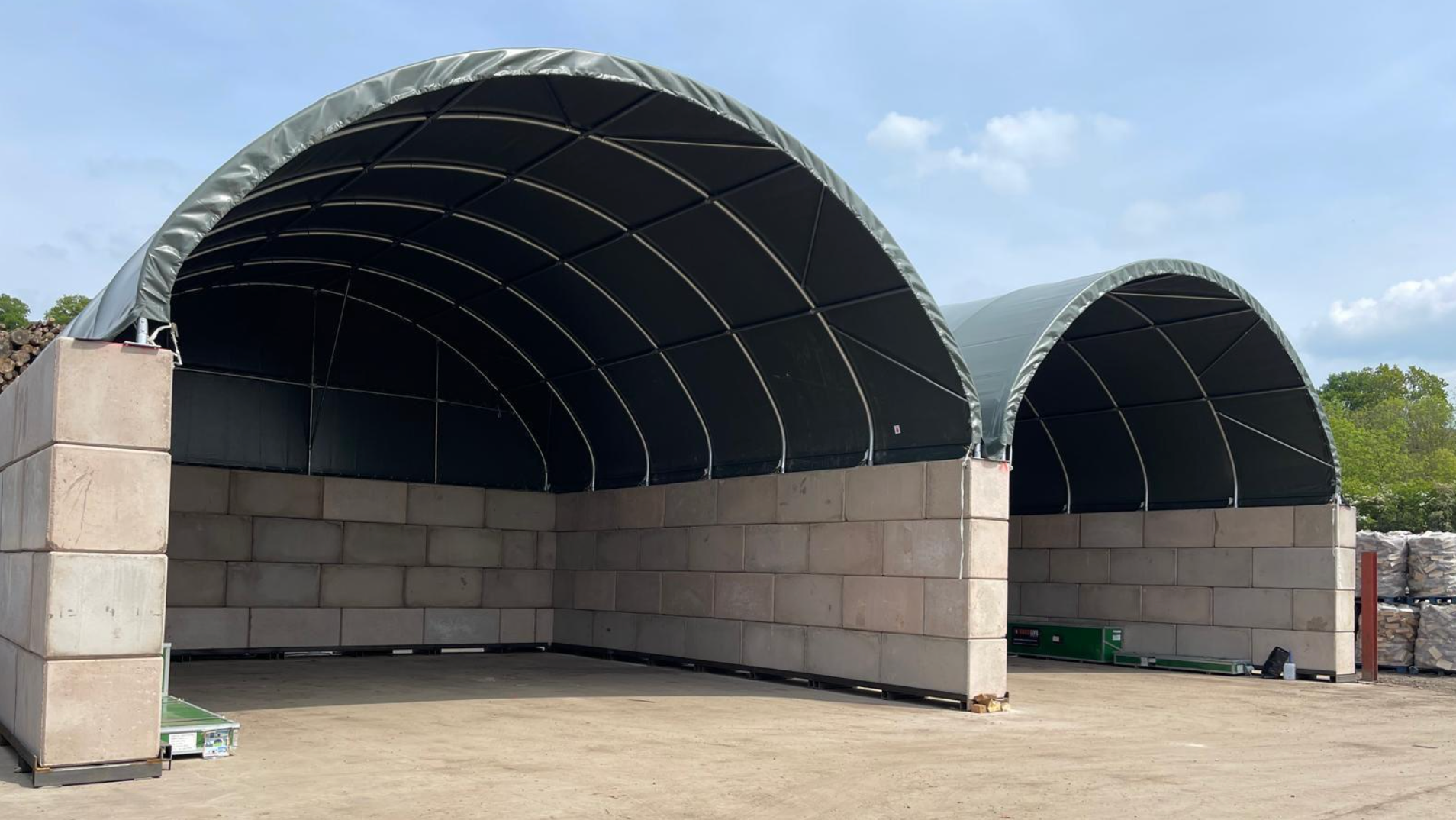 Large fabric-covered storage structure with concrete walls on a clear day.